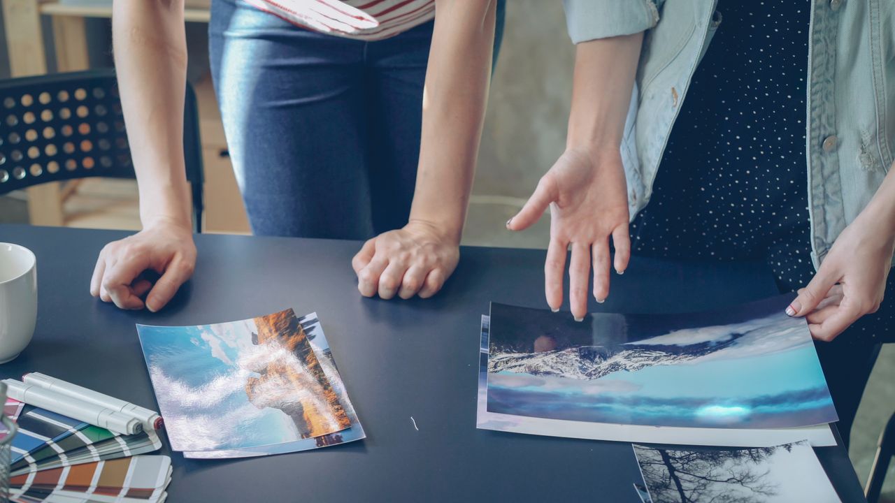 Two people analyzing printed landscape photographs on a table indoors.